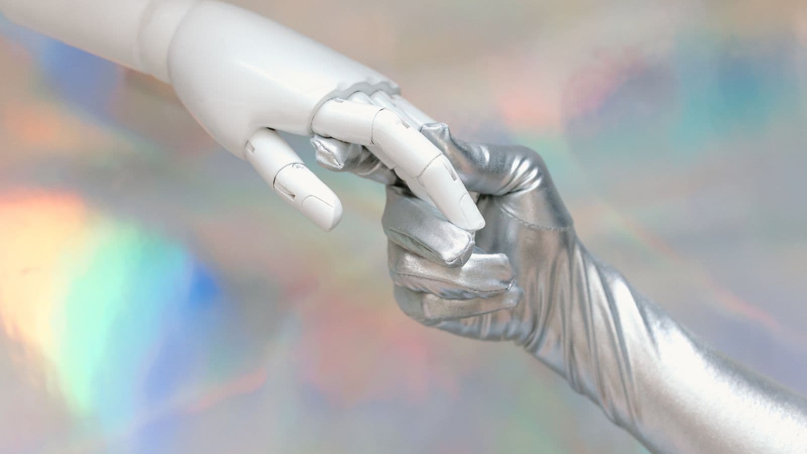 White robotic hand touching a hand in a silver glove against an iridescent background