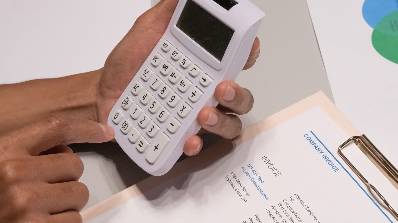 Close-up of hands using a calculator beside an invoice on a desk
